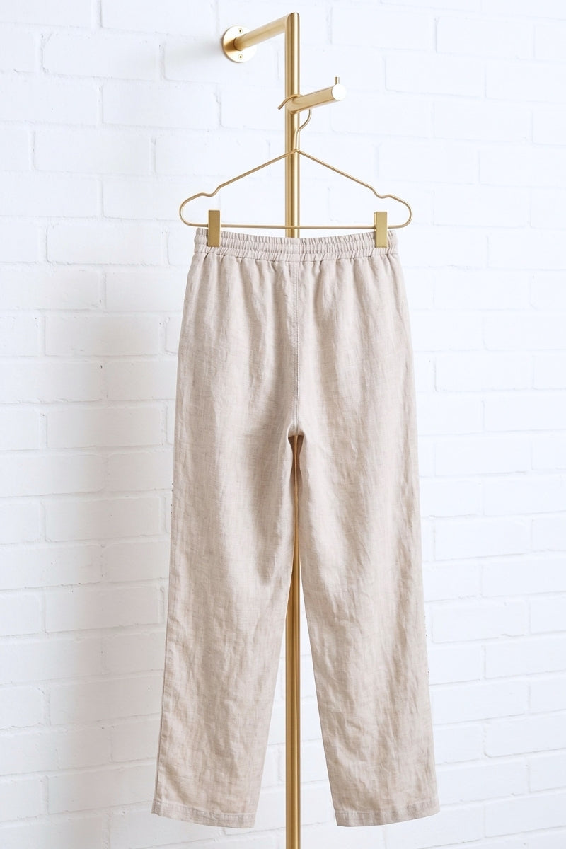 Beige pants hanging on a gold hanger against a white brick wall.