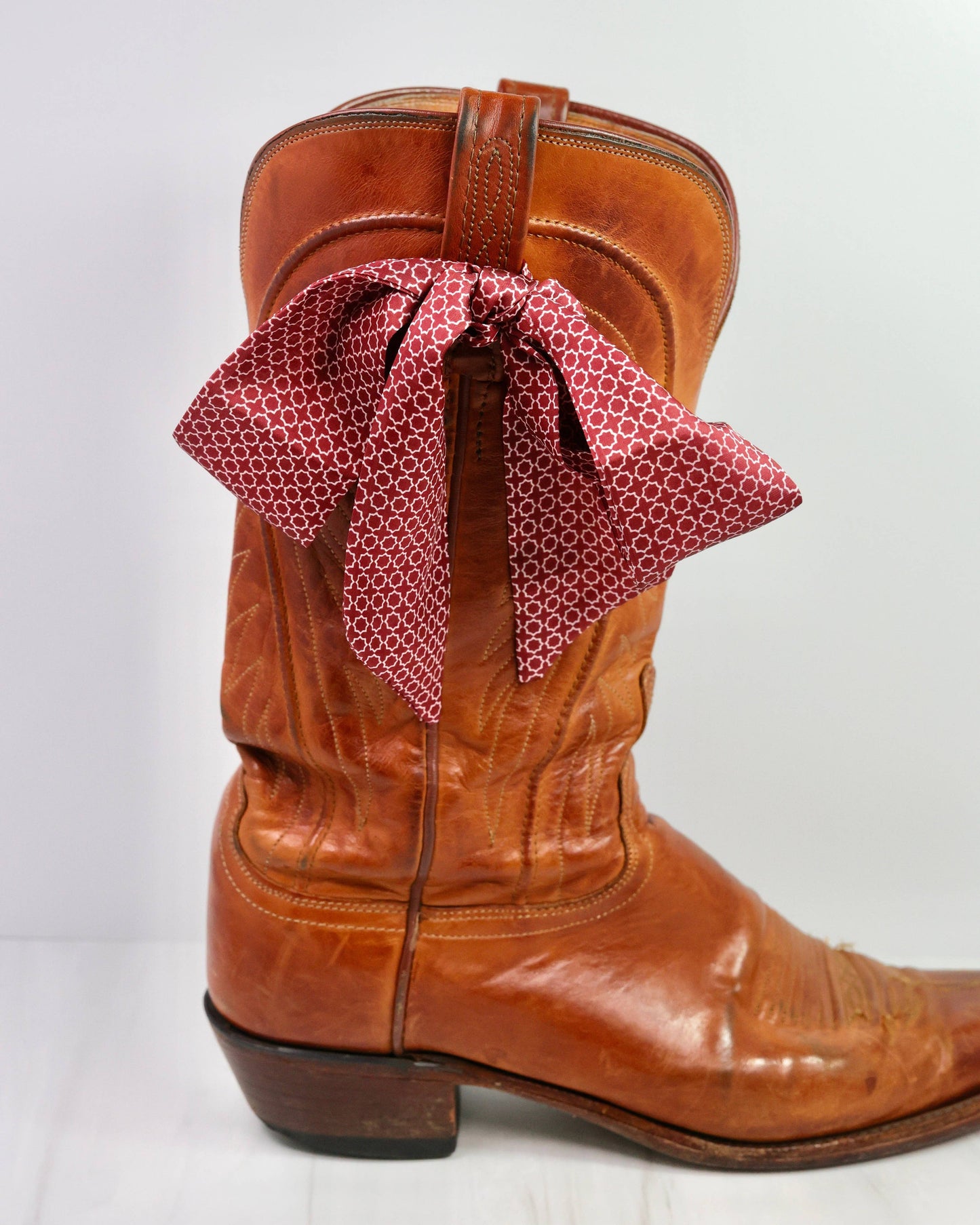 Brown cowboy boot with a red patterned bandanna on a white background