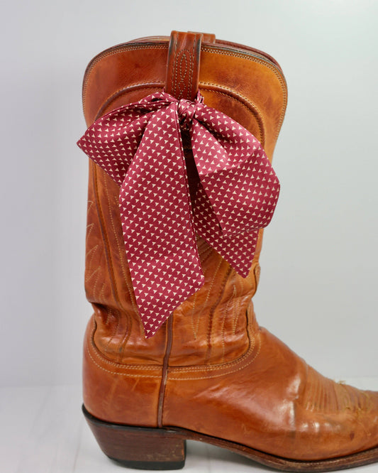 Brown cowboy boot with a red polka dot bow on a light gray background