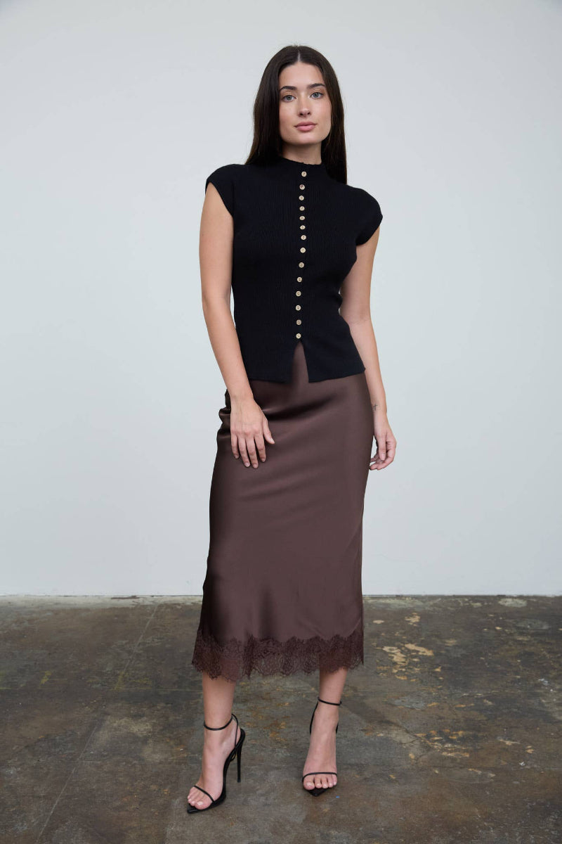 Woman wearing a black top with buttons and a brown skirt on a plain background