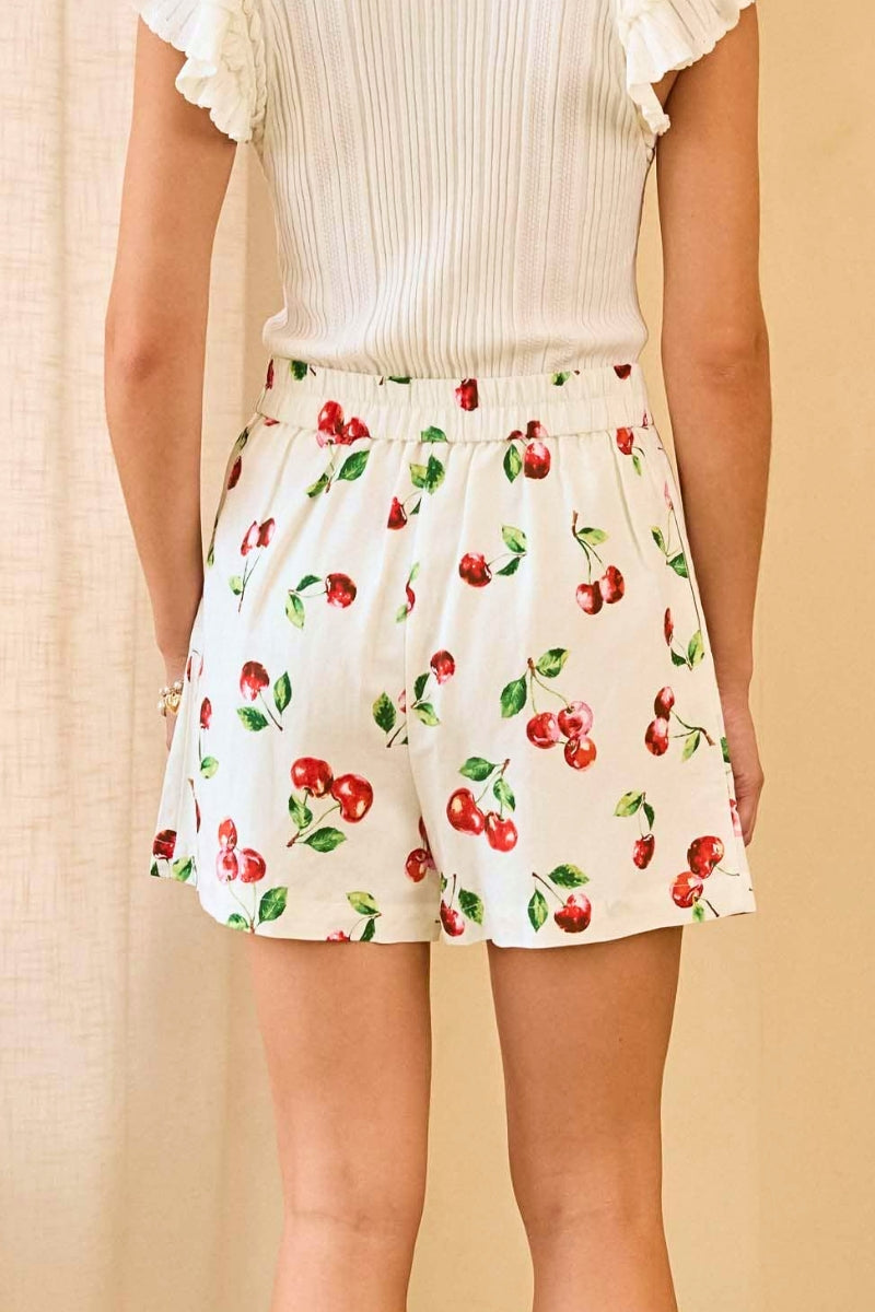 Person wearing a white blouse and cherry-patterned shorts against a beige background