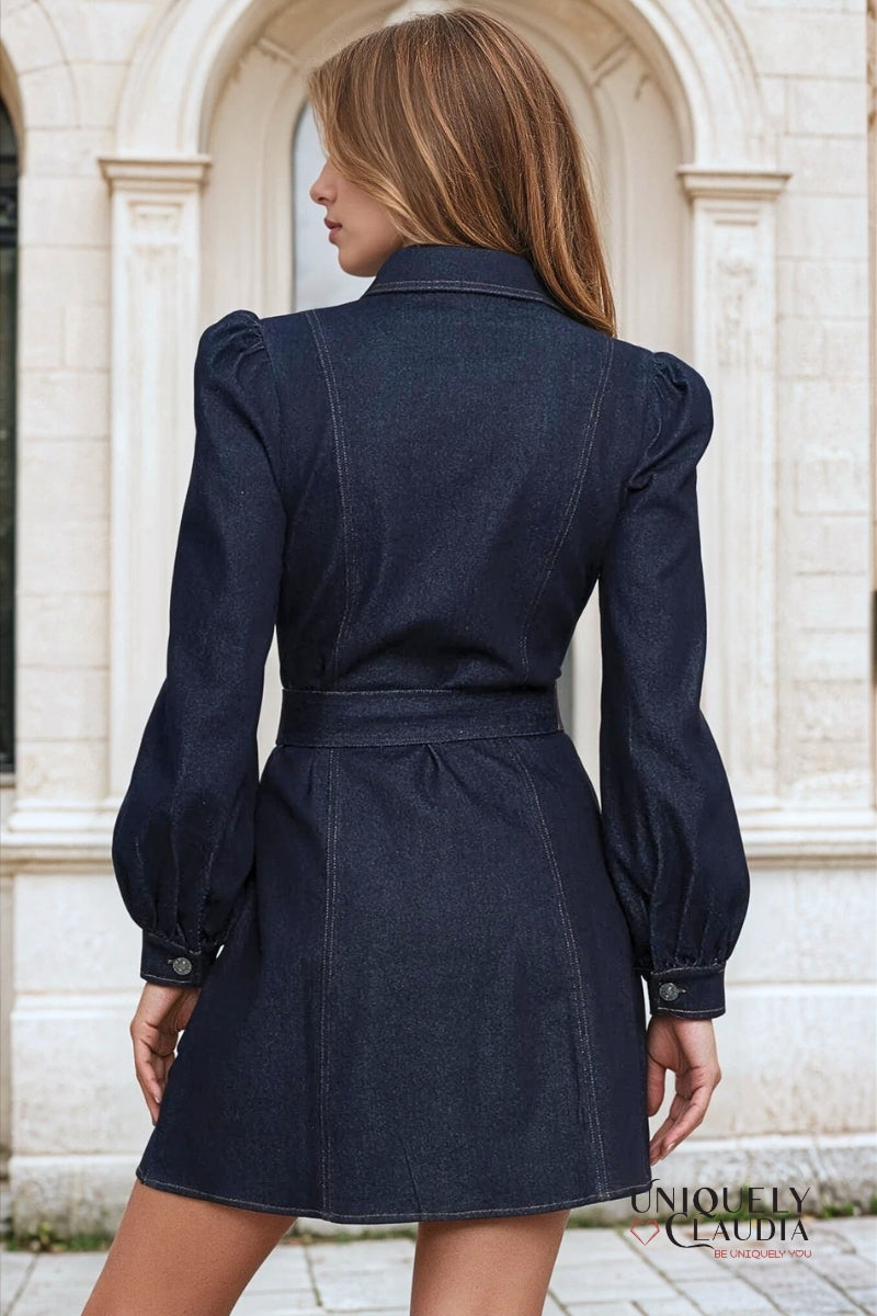 Woman wearing a dark denim dress with puffed sleeves in front of an architectural background.