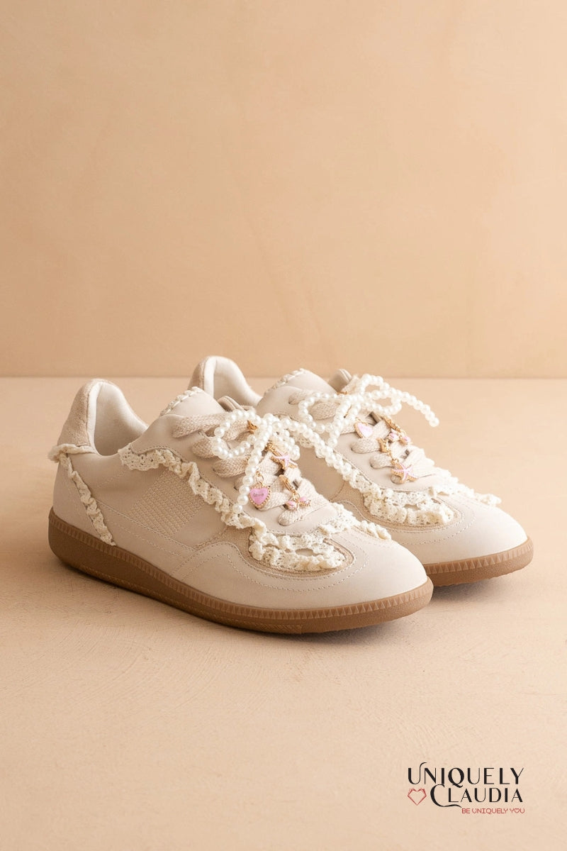 Pair of white sneakers with lace details on a beige background