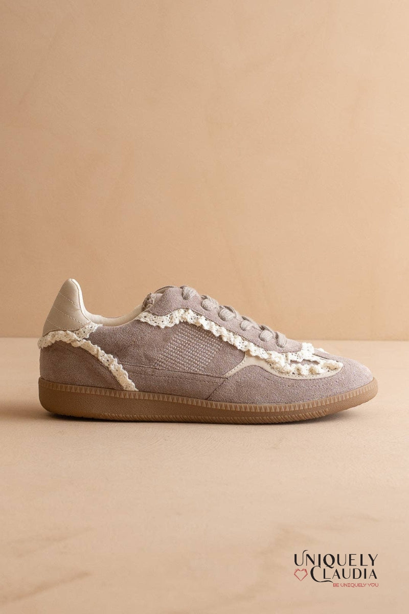 Gray sneaker with white lace details on a beige background, featuring the brand 'Uniquely Claudia'.