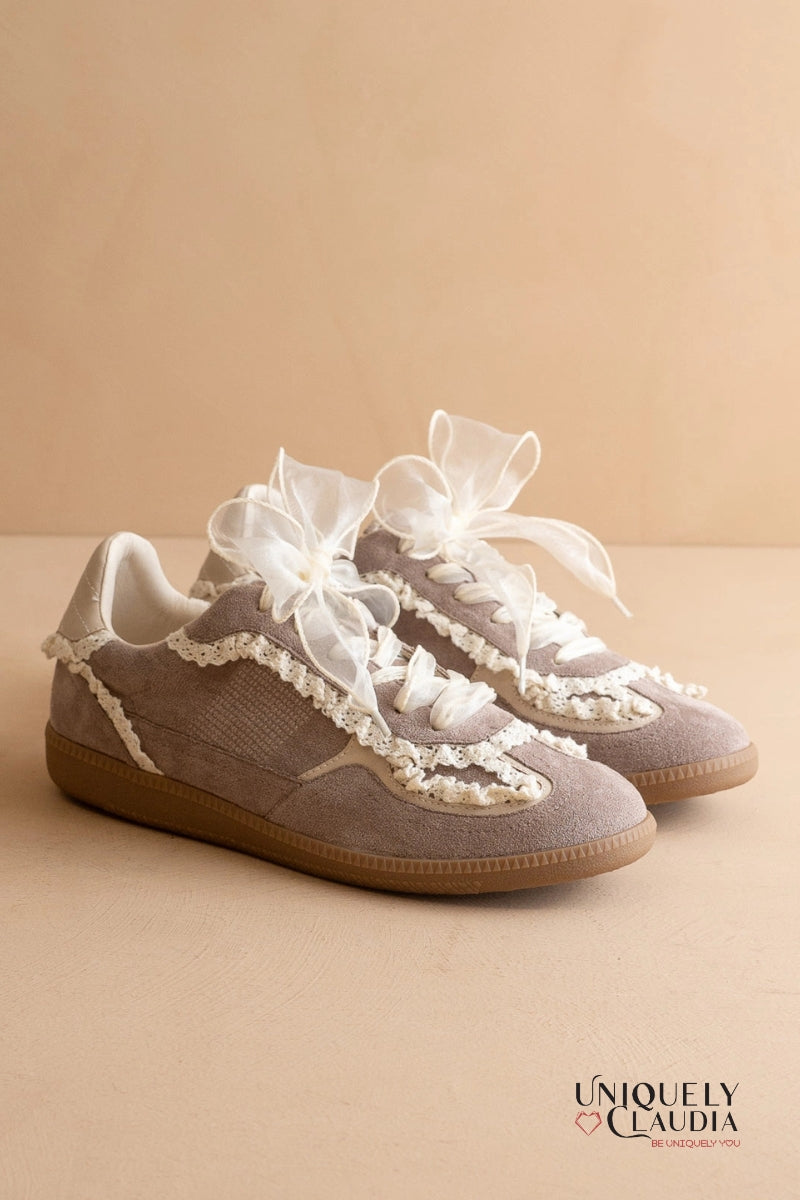 Pair of sneakers with lace details on a beige background, branded 'Uniquely Claudia'.