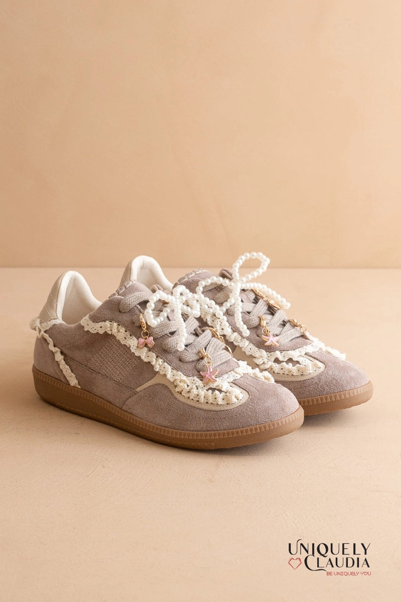 Pair of gray sneakers with white laces on a beige background, featuring the brand 'UNIQUELY CLAUDIA'.