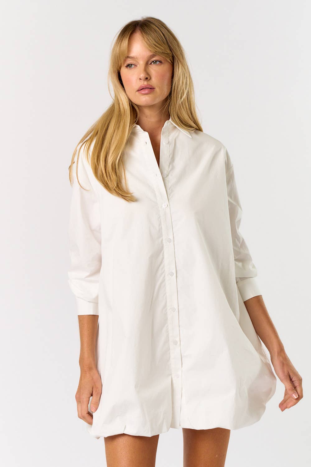 Woman wearing a white shirt dress against a plain background
