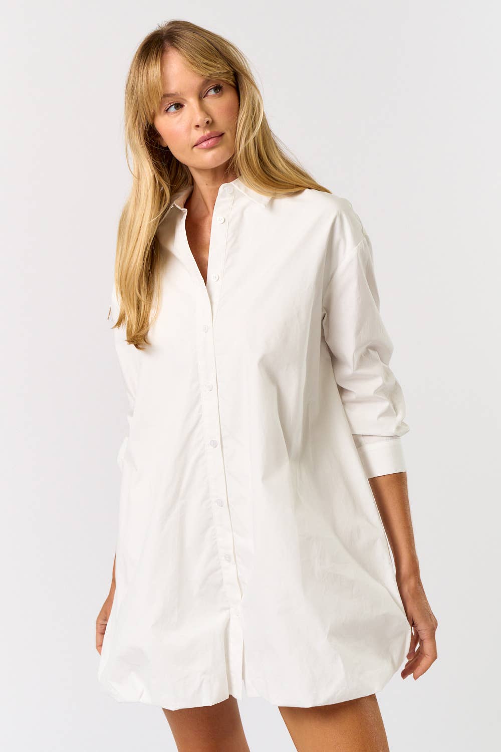 Woman wearing a white shirt dress against a plain background