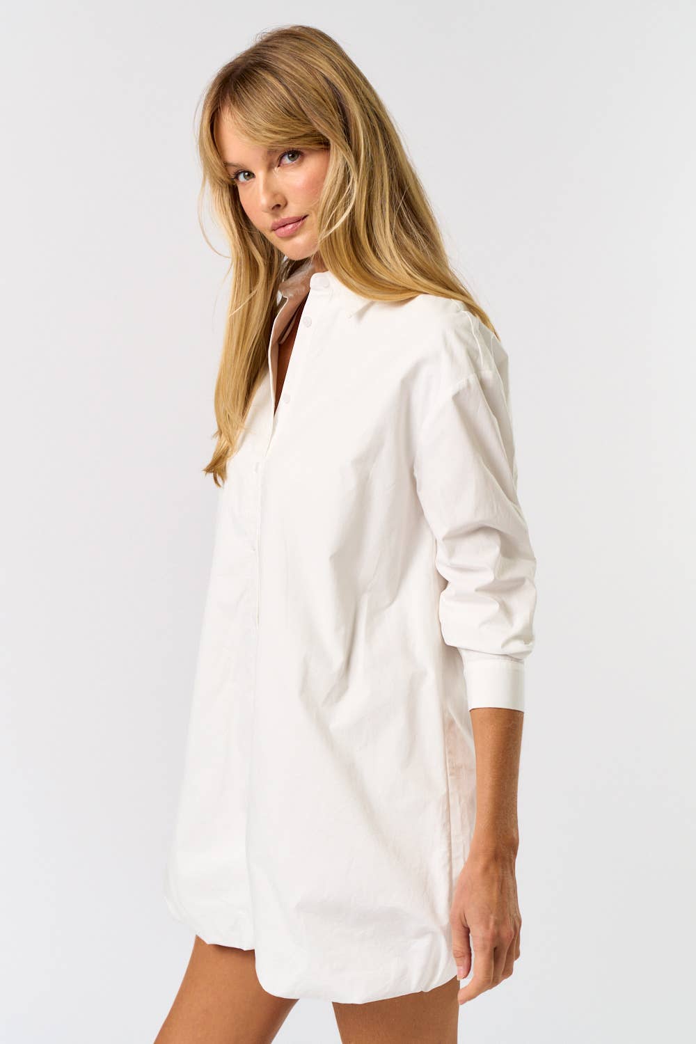 Woman wearing a white shirt dress against a plain background