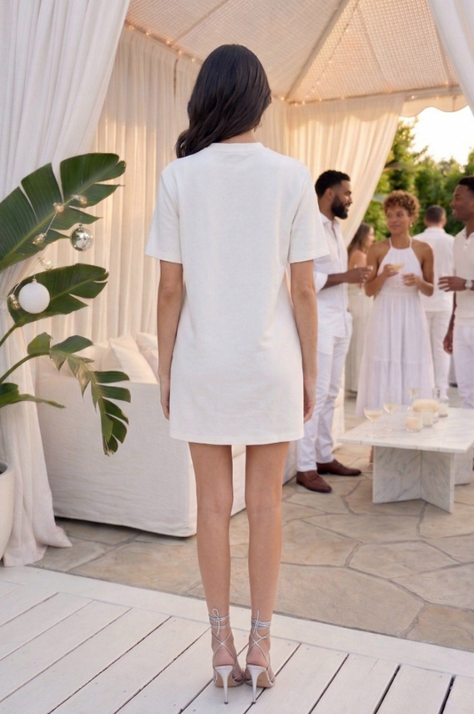 Woman in a white dress standing in front of a white canopy with people in the background.