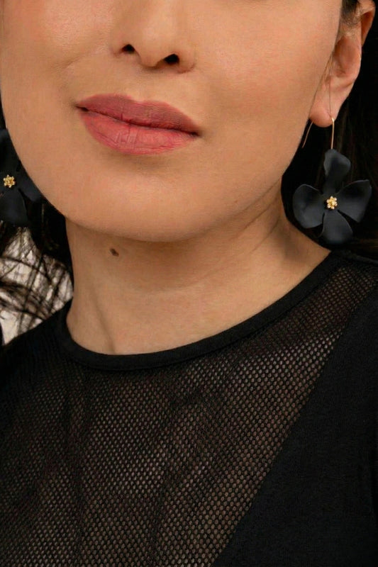 Close-up of a person wearing black floral earrings with gold centers.
