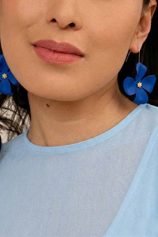 Close-up of a person wearing blue earrings with floral designs.