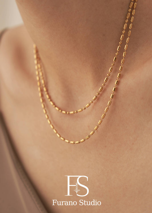 Gold necklace on a person's neck with 'Furano Studio' logo.
