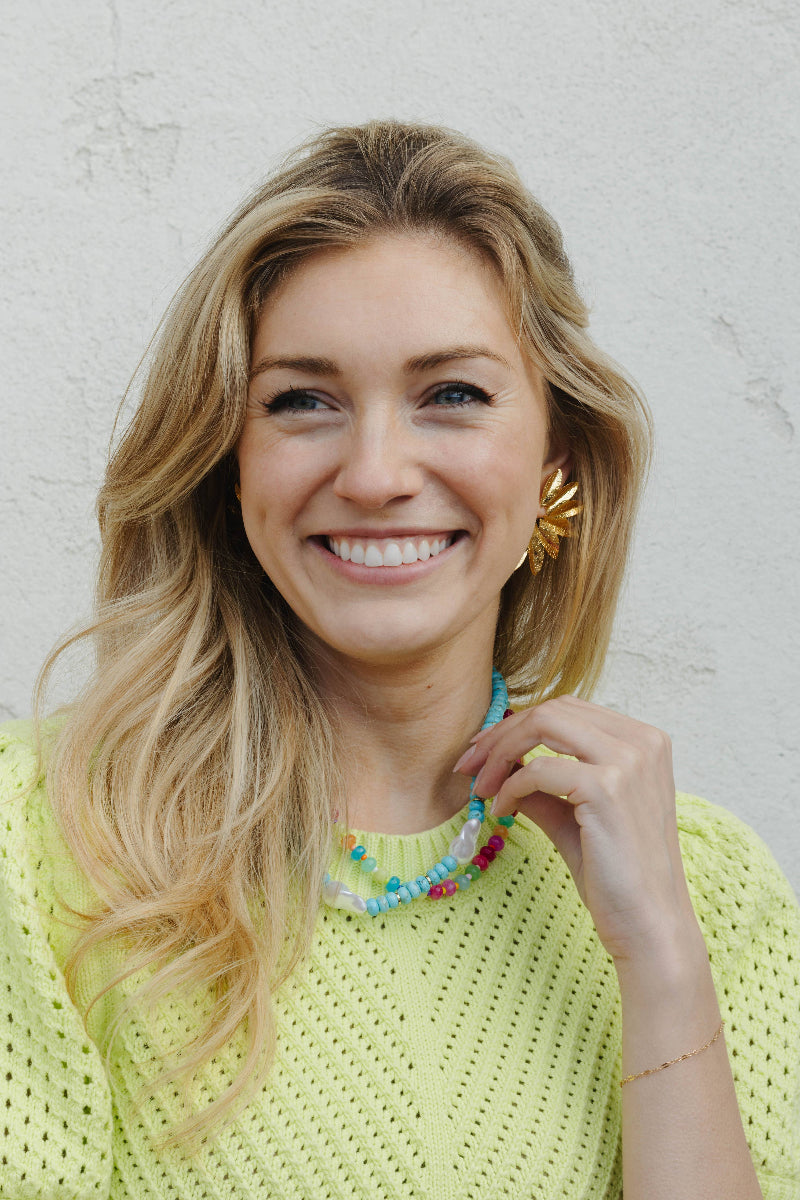 Woman wearing a colorful necklace and smiling against a light background
