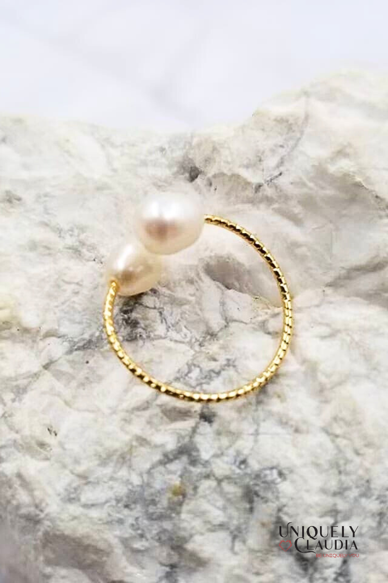 Gold ring with a pearl on a marble surface, branded 'Uniquely Claudia'.