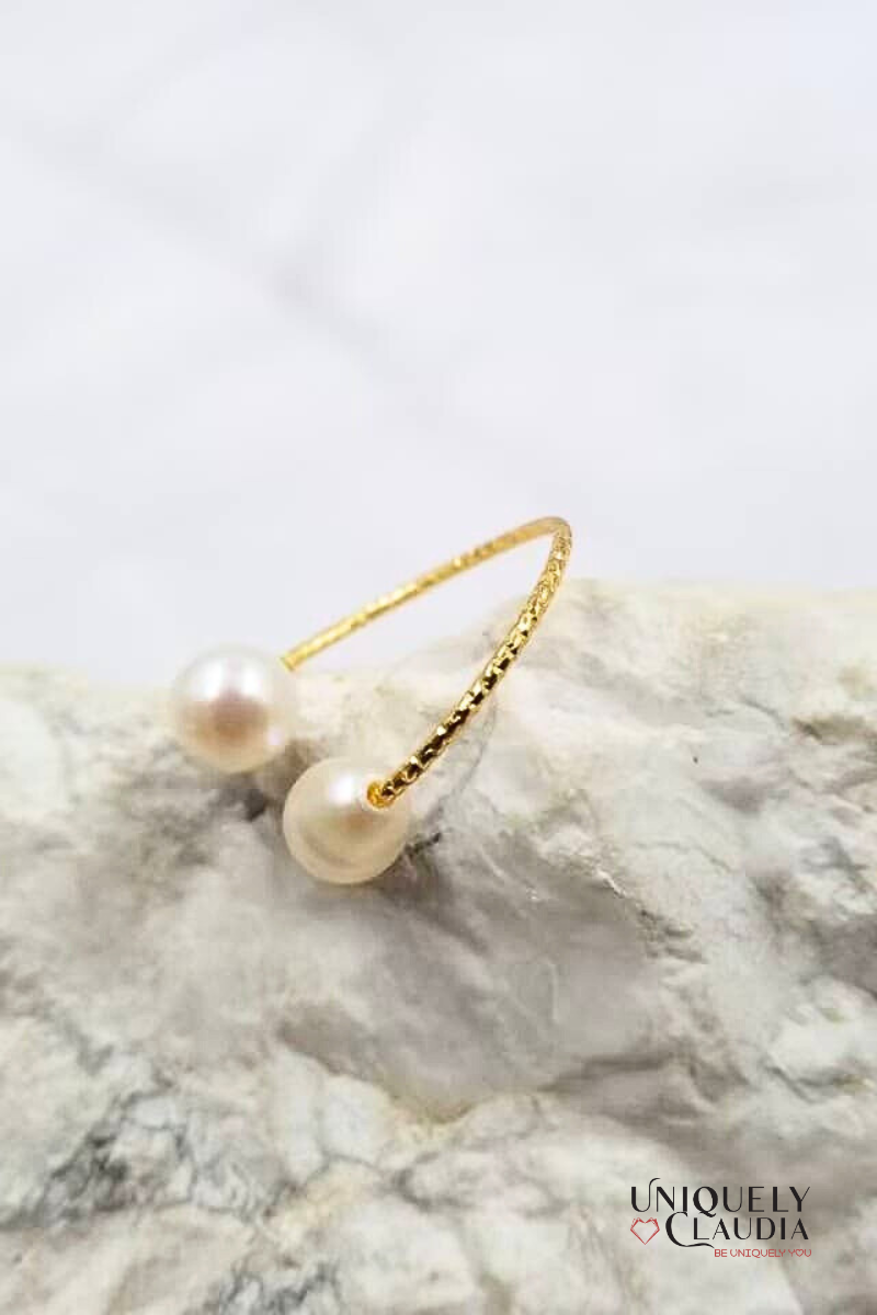 Gold ring with pearls on a marble surface, branded 'Uniquely Claudia'.