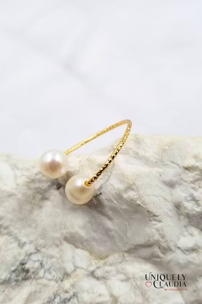 Gold ring with pearls on a marble surface, branded 'Uniquely Claudia'.