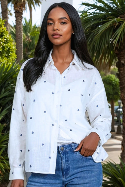 Woman wearing a white blouse with blue hearts patterns and blue jeans outdoors.