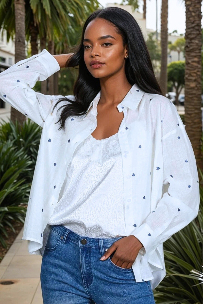 Woman wearing a white blouse with blue hearts patterns and blue jeans outdoors.