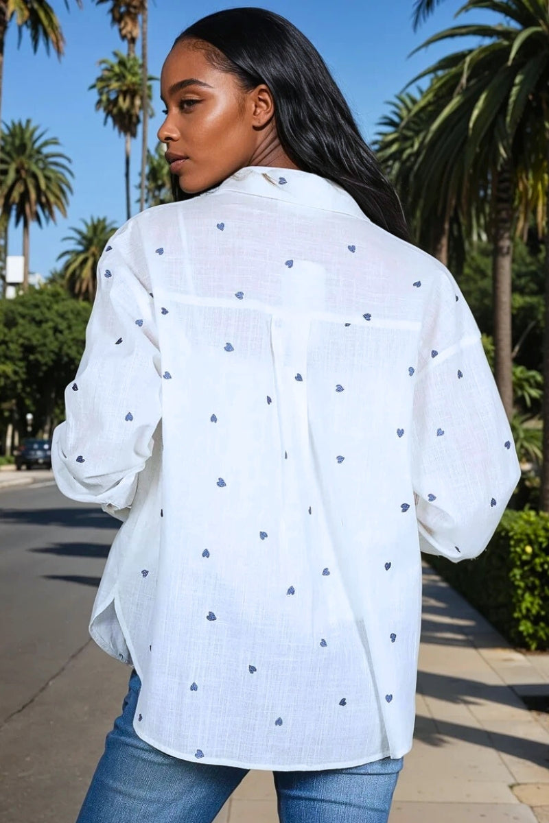 Woman wearing a white blouse with blue hearts patterns and blue jeans outdoors.