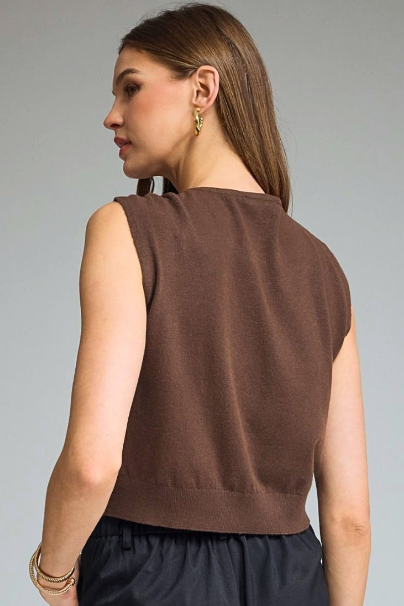 A woman shown from the back wearing a sleeveless brown knit top and dark navy bottoms, photographed against a plain light gray studio background.
