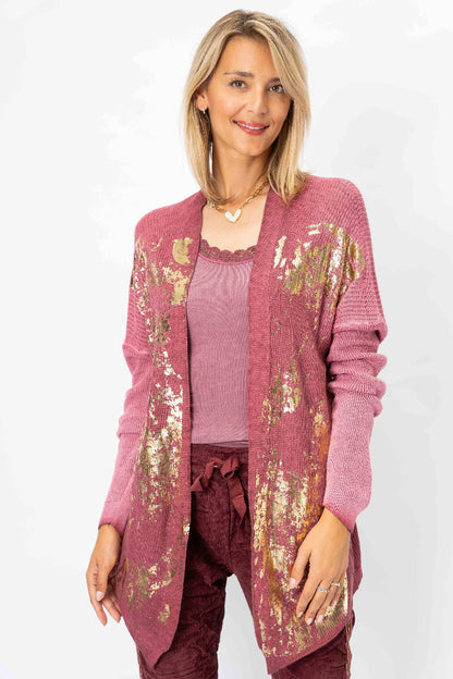 A woman modeling a dusty rose open-front cardigan with gold sequin patterns, worn over a matching dusty rose top and burgundy pants, against a plain white background.