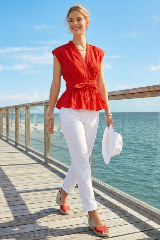 Woman in a red top and white pants walking on a wooden pier by the sea.