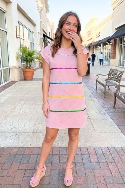 Woman in a pink dress with colorful stripes standing on a sidewalk.