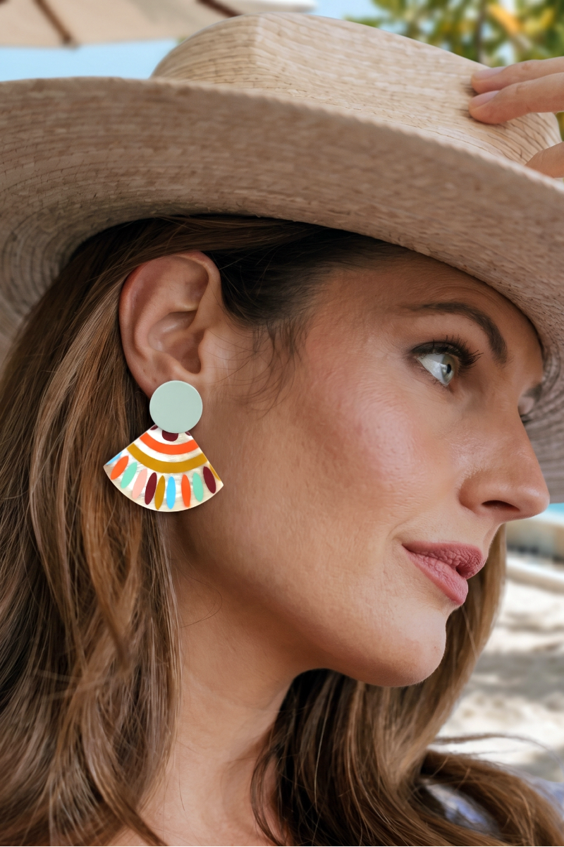 Woman wearing a wide-brimmed hat and colorful earrings with a beach in the background