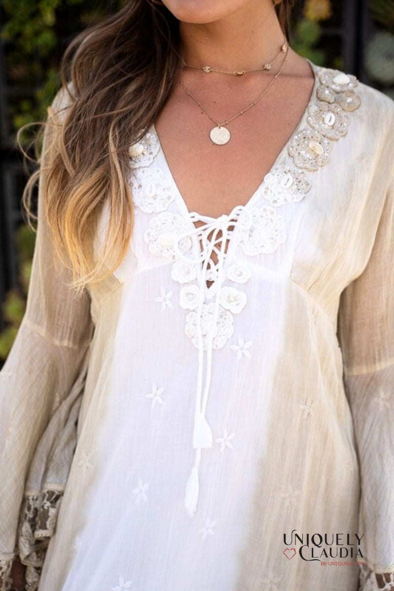Woman wearing a white lace-up top with sheer beige cardigan, surrounded by greenery.