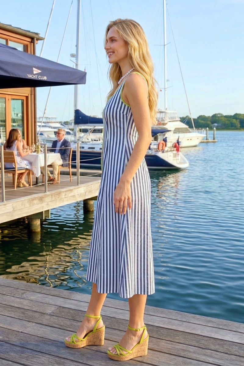 Woman in a striped dress standing on a dock with boats in the background