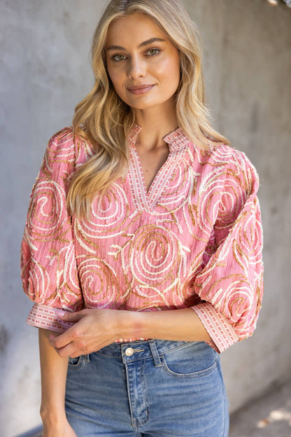 Woman wearing a pink patterned blouse and blue jeans against a neutral background