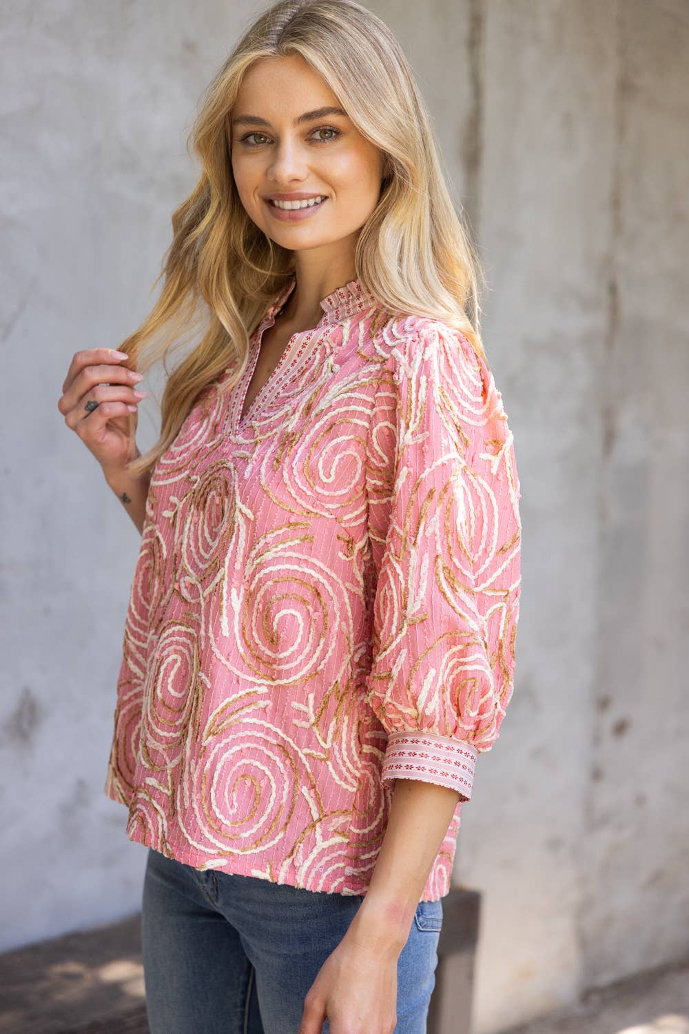 Woman wearing a pink patterned blouse against a gray concrete wall.