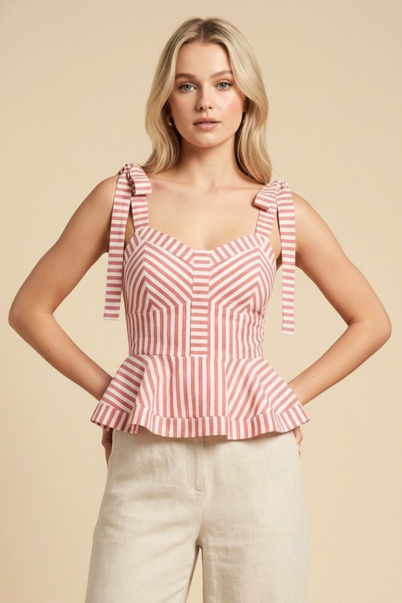 Woman wearing a pink and white striped top with ruffled straps on a beige background