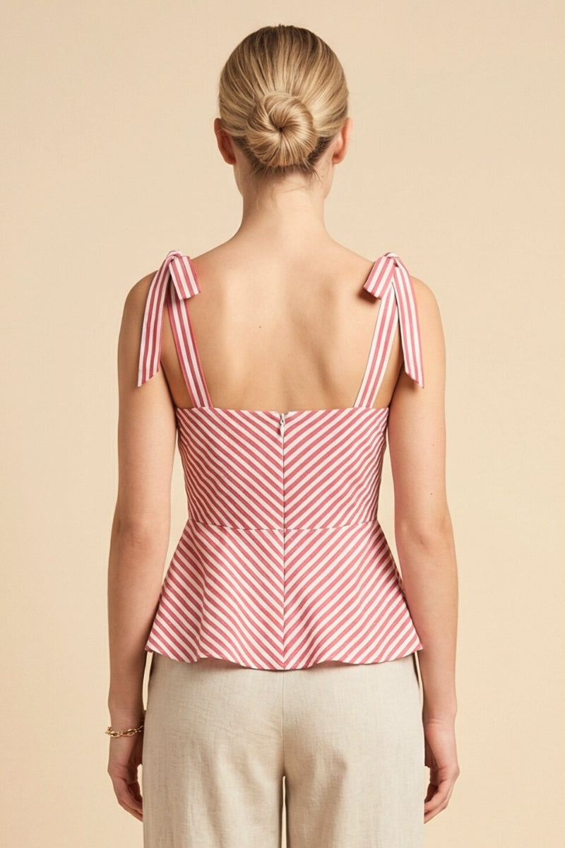 Woman wearing a pink and white striped top with bow straps on a beige background