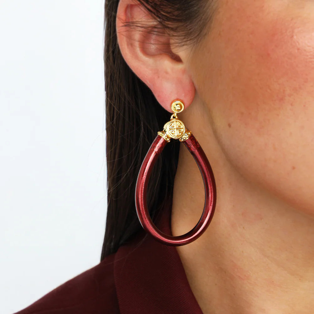 Red hoop earring with gold accent worn by a person on a white background