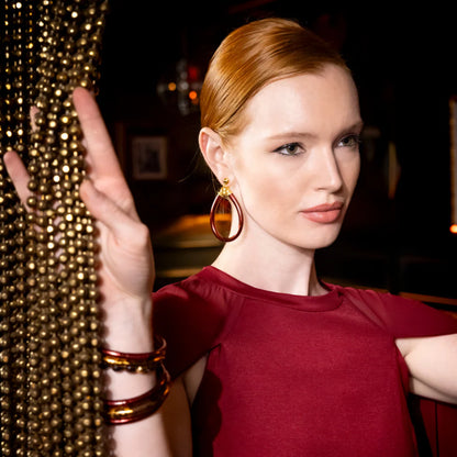 Woman in a red dress with gold jewelry and accessories, posing against a dark background.
