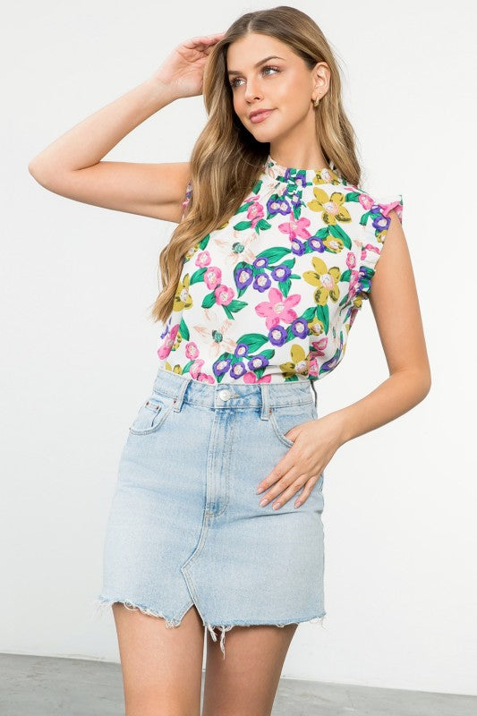 Woman wearing a colorful floral top and denim skirt against a white background