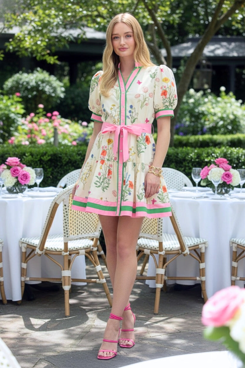 Woman in a floral dress standing outdoors with tables and flowers in the background