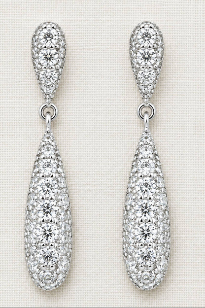 A pair of silver teardrop dangle earrings paved with clear cubic zirconia stones, displayed on a textured off-white fabric background.