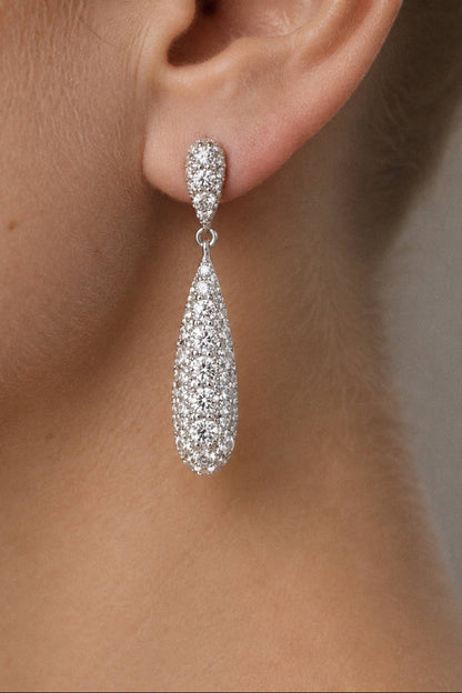 A close-up of a model's ear wearing a teardrop-shaped silver dangle earring encrusted with clear pavé stones.