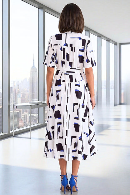 Woman wearing a patterned dress in an office setting with a cityscape view.