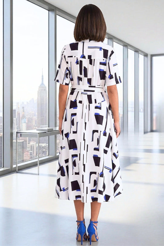 Woman wearing a patterned dress in an office setting with a cityscape view.