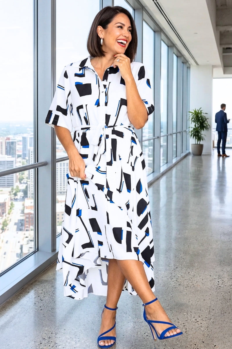 Woman in a stylish dress standing in a modern office building with large windows.
