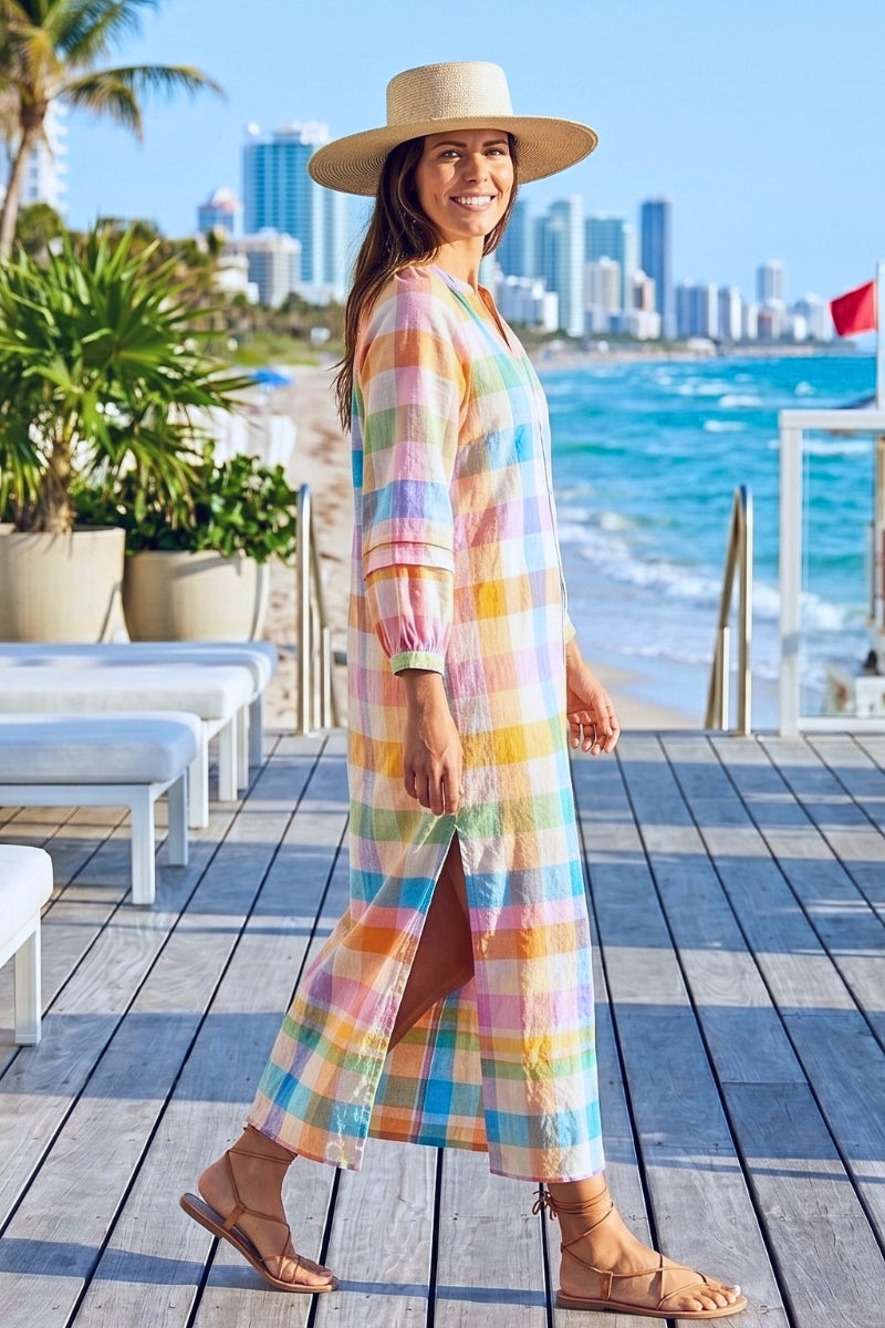 Woman in a colorful dress and hat standing on a deck with ocean and city skyline in the background