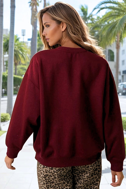 Woman wearing a maroon sweatshirt with palm trees and a street in the background