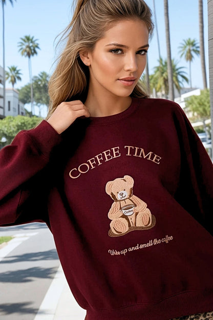 Woman wearing a maroon sweatshirt with a teddy bear and 'Coffee Time' text, palm trees in the background.