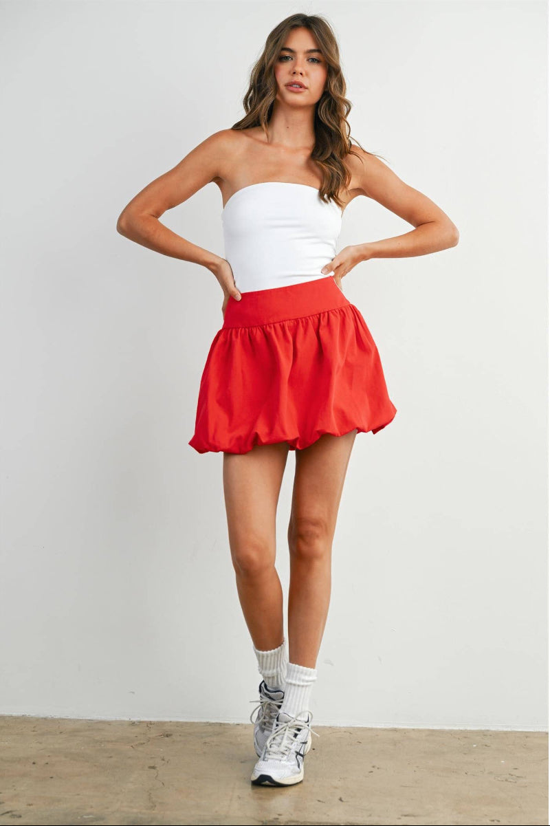 Woman wearing a white top and red skirt against a plain background