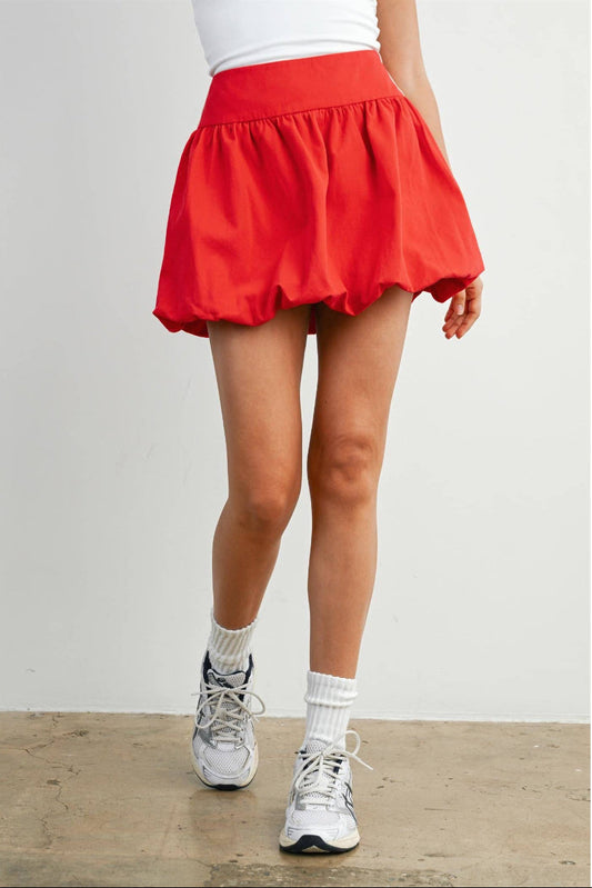 Woman wearing a red skirt with white sneakers and socks on a plain background