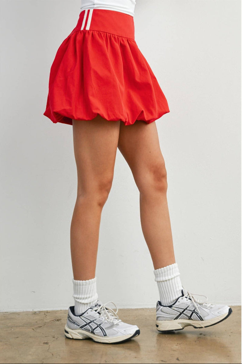 Woman wearing a red skirt, white socks, and gray sneakers on a plain background